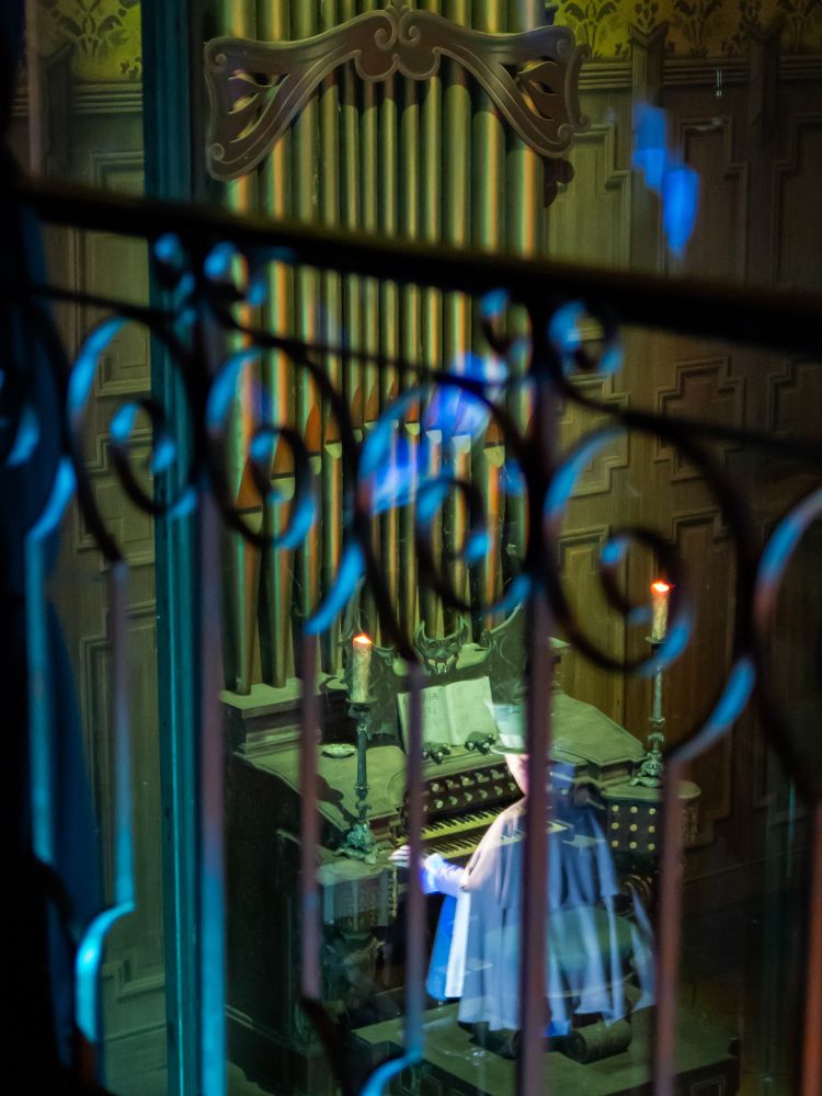 A ghostly organist plays an organ in the distance through a wrought-iron railing.