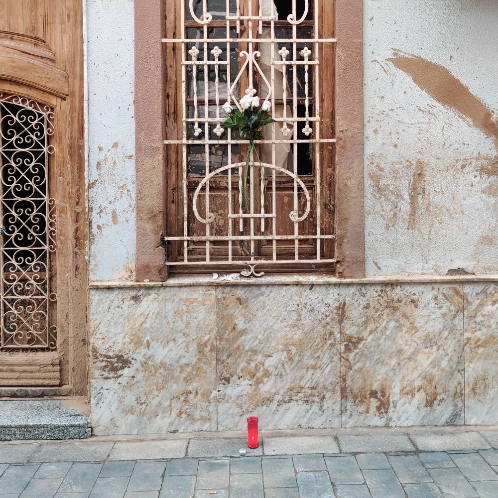 una espelma i flors blanques en la finestra d'una casa de Paiporta