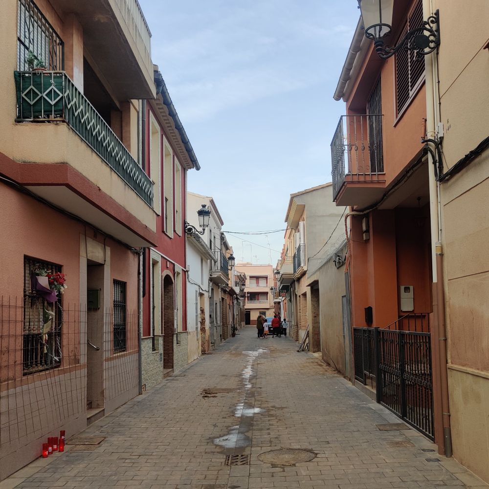 el carrer Benlliure de Paiporta 30 dies després de la Dana, sense trastos ja al carrer. se veu una porta a l'inici amb flors i espelmes en record de persones que han mort en eixa casa