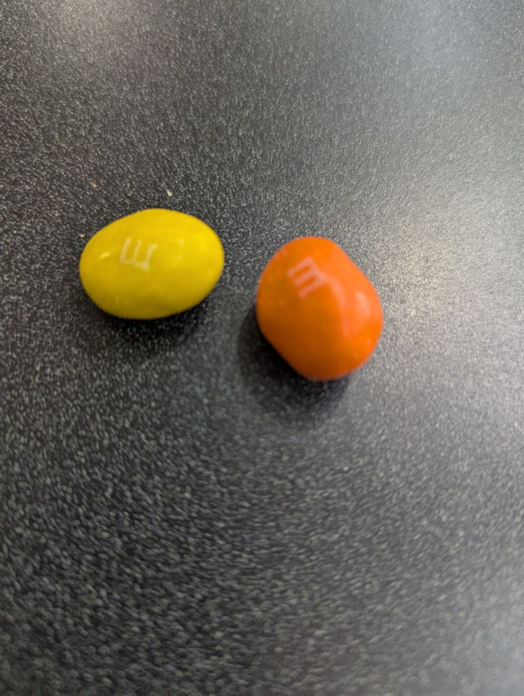 A photo of two fat M&Ms, one is yellow and the other is orange.