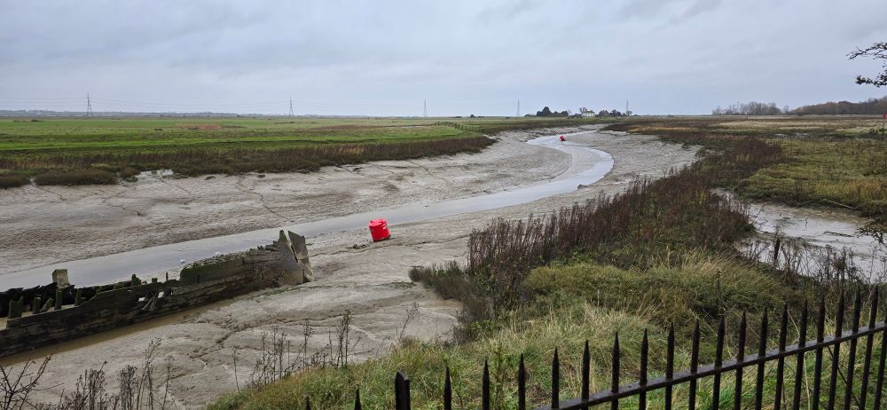 Viewing along Faversham Creek with an old wreck to the left and a couple of red buoys visible. I'm sheltered under bushes away from the rain and wind. The tide was out, and there were roosting Black-headed and Herring Gulls. Also, there were feeding Redshank, Teal, Little Grebe, and Cormorant. It was also here that the Grey Wagtail and Greenshank flew through.