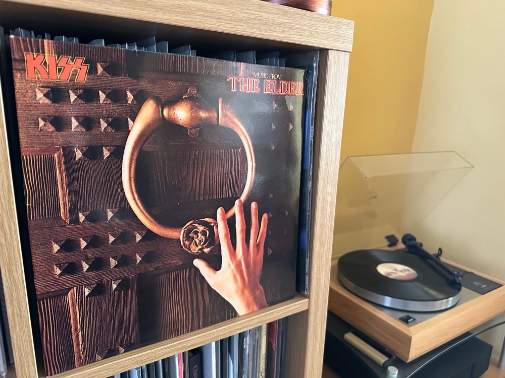 Cover of the Kiss album Music from The Elder” which depicts a hand reaching for a large brass door knocker on a studded wooden door.