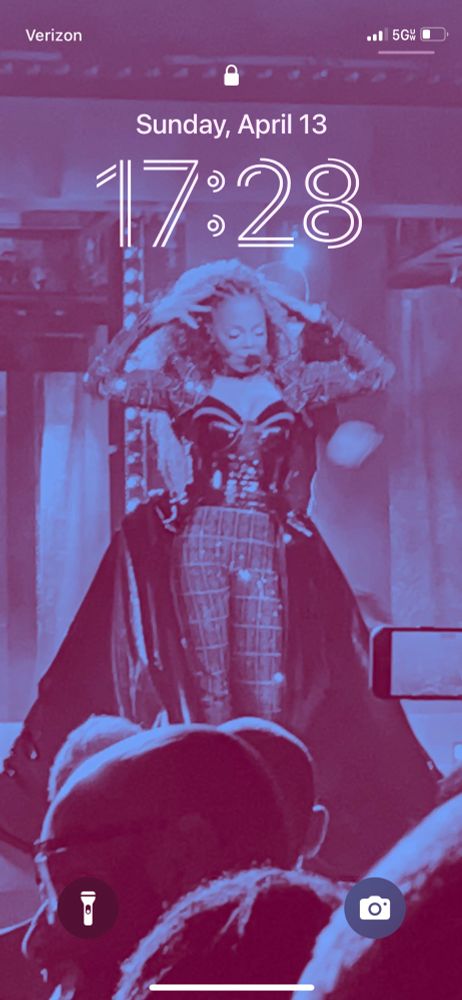 Screenshot of iPhone Lock Screen. Picture of Janet Jackson with arms up in blue. Time displayed is 17:28. 