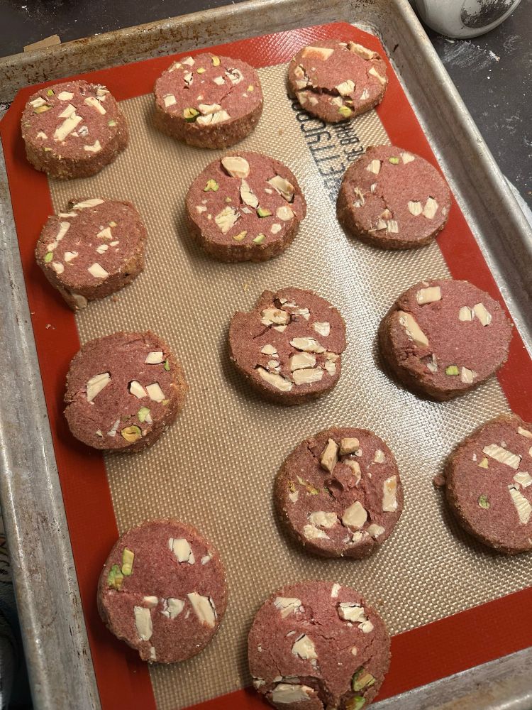 A baker’s dozen of cooked cookies that look like mortadella because they are pink and have white chunks and pistachios in them. 