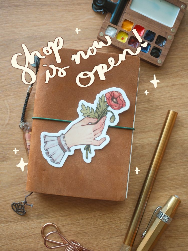 Photo featuring a vinyl die cut sticker of a hand holding a poppy flower. “Shop is now open” is written in cursive above.