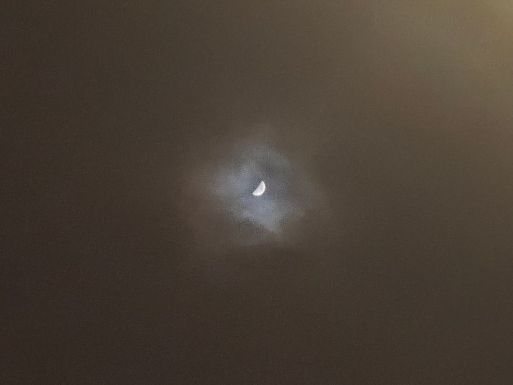 Low-res photo of a waxing crescent moon peeking through a hole in the clouds.