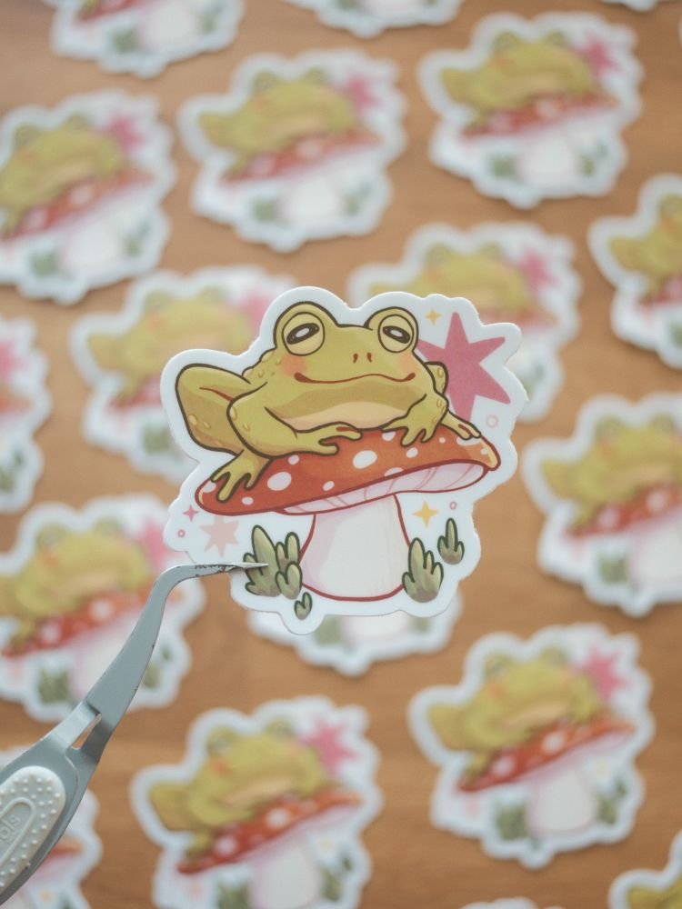 die cut sticker of a frog sitting contentedly upon a mushroom