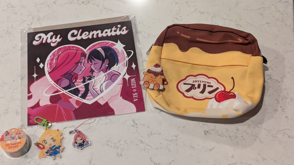 A delivery from artist Joylychi, featuring an Alien Stage print and phone strap charm, a Marcille keychain and Dungeon Meshi washi tape, and a pudding-inspired crossbody bag.