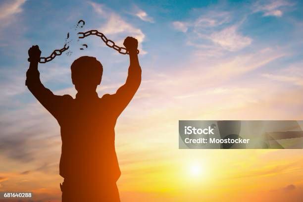 Stock photo of man in a sun set with his hands in the air breaking his chained braces