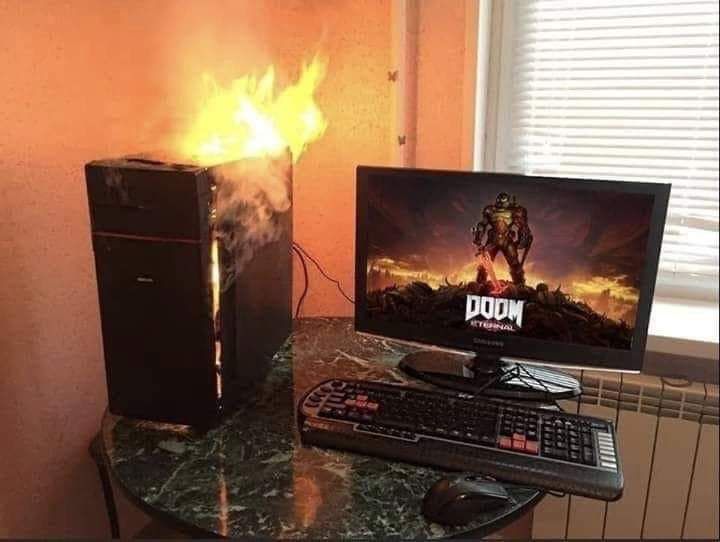 an image of a desktop computer on fire while the monitor is showing a picture of Doom Eternal