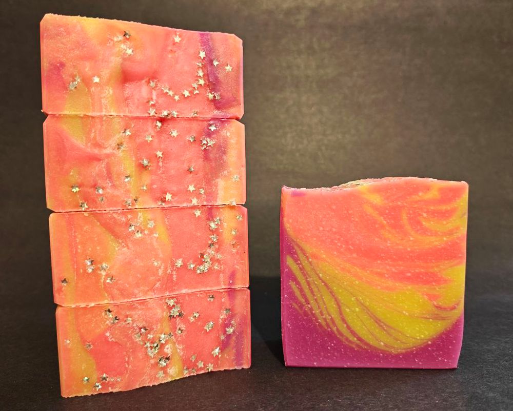 One the left four bars of neon pink, yellow and purple soap are stacked on their side to show the biodegradable star shaped glitter. On the right is a single bar showing the feathered design
