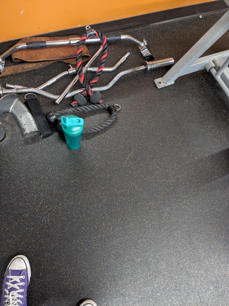 A photo taken at the gym. My purple high tops are just visible in the left corner. A pile of cable equipment is in the middle with a greenish water bottle