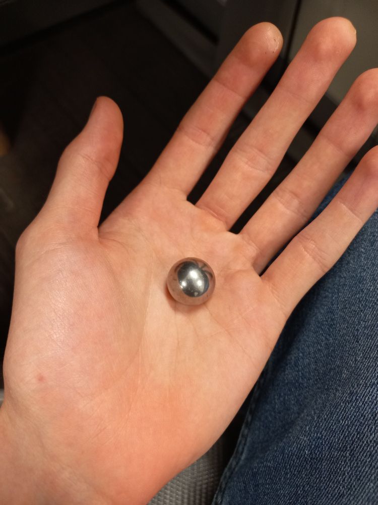 me holding a large metal ball bearing about the size of a marble.