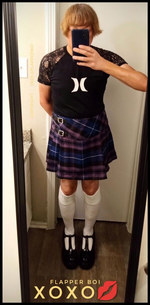 Femboy wearing a black lace rash guard made by Hurley, which is a very rare item, by the way, and a purple and blue Billie mini kilt with the Pride of Scotland tartan, with white knee socks and black patent leather Mary Jane shoes.