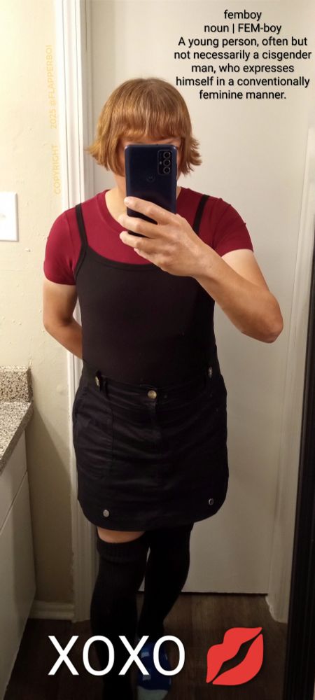 A dictionary definition of the word Femboy with a picture of a femboy wearing a reddish bobbed haircut, and a Burgundy red short sleeve bodysuit under a black camisole and a black pencil skirt, plus black thigh high socks.