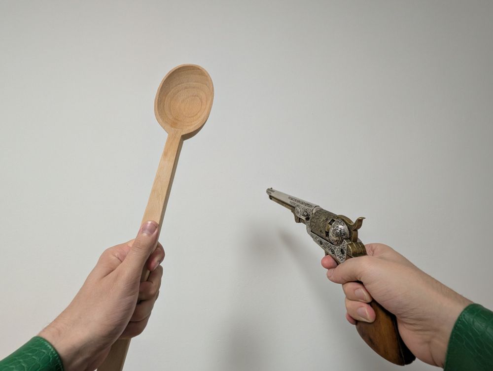 First Person POV, with left hand holding a big wooden spoon and right hand holding a replica of an engraved 1851 Colt Navy