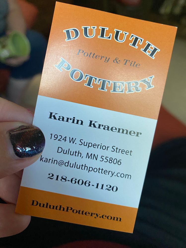 A business card in orange and white. “Duluth Pottery. Karin Kraemer. 1924 W. Superior Street, Duluth MN 55806. Karin @ DuluthPottery.com. 218-606-1120. DuluthPottery.com”