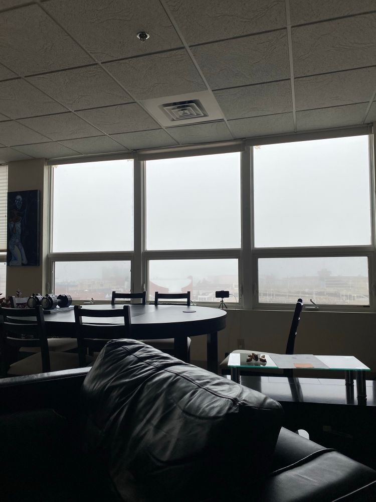 A chair and table in the foreground, looking out windows towards Duluth harbor with only the haze of buildings visible through the fog 
