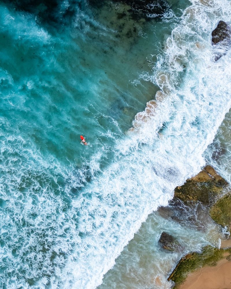 A birds eye view of a single surfer swimming out to catch some waves 