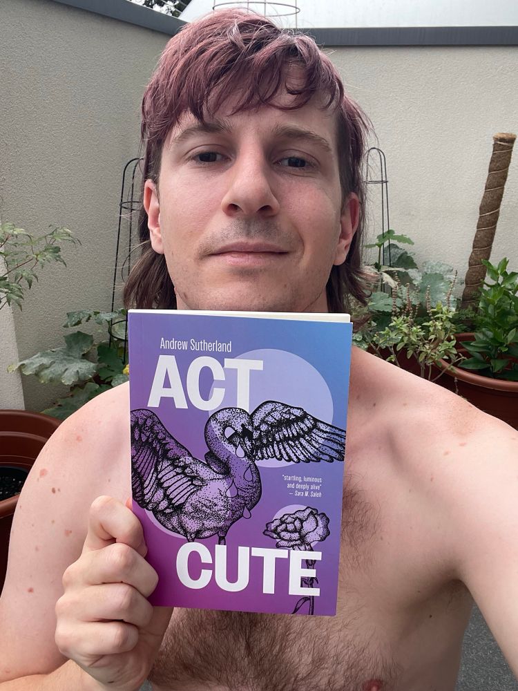 A photograph of me, a white person with dark purple hair, holding a copy of my book. The cover is purple and blue, with an illustration of a swan, a flower, and in bold white font the title ACT CUTE. 