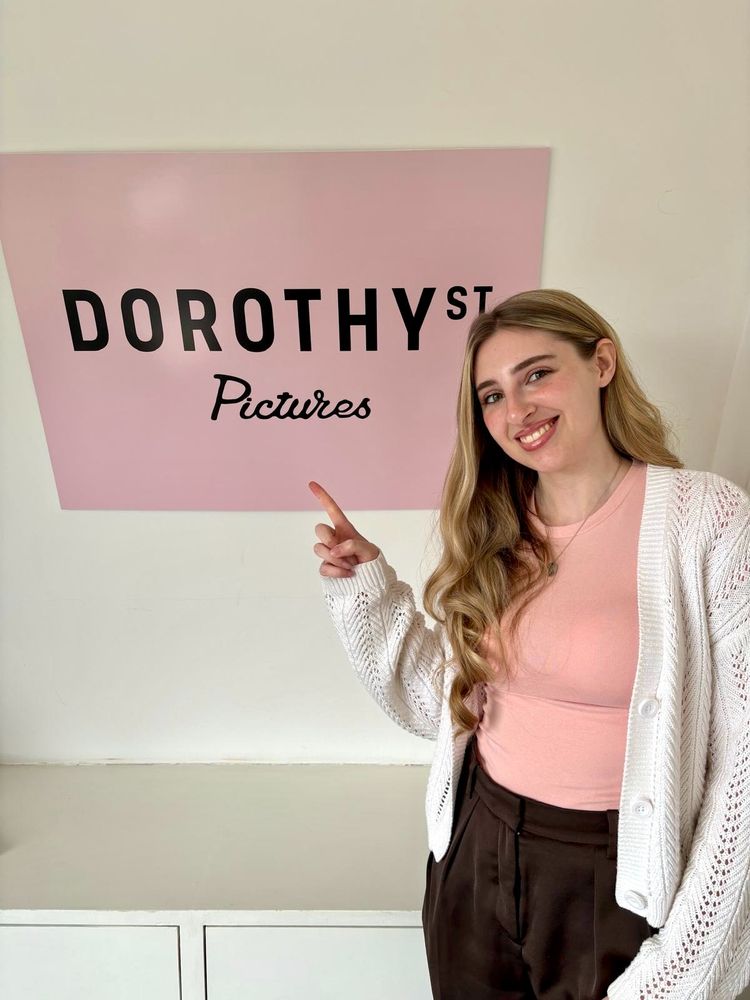 Jess stands and points to the Dorothy St Pictures poster on the wall behind her