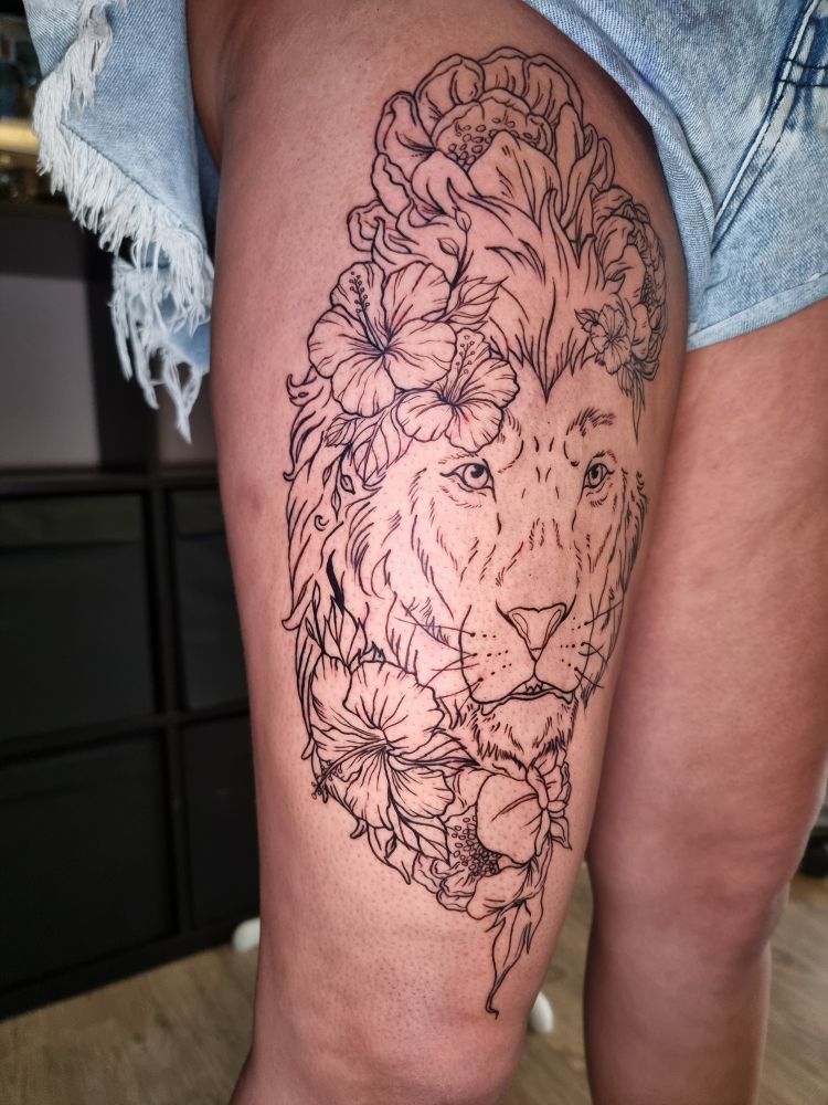A floral lion linework tattoo on the upper thigh.