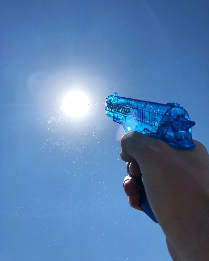 A clear blue water gun being fired at the sun