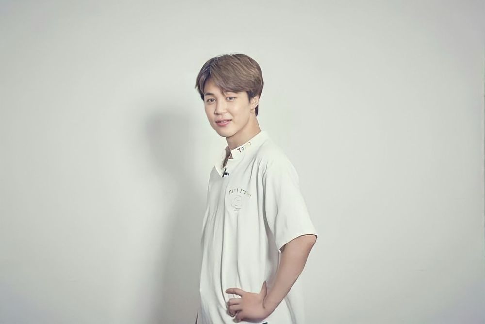 Jimin in a white shirt standing in front of a white wall