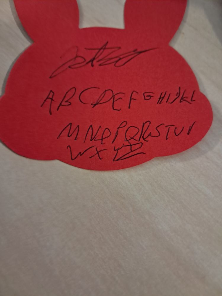 A very sloppily written alphabet written on a red note pad shaped like a bunny.