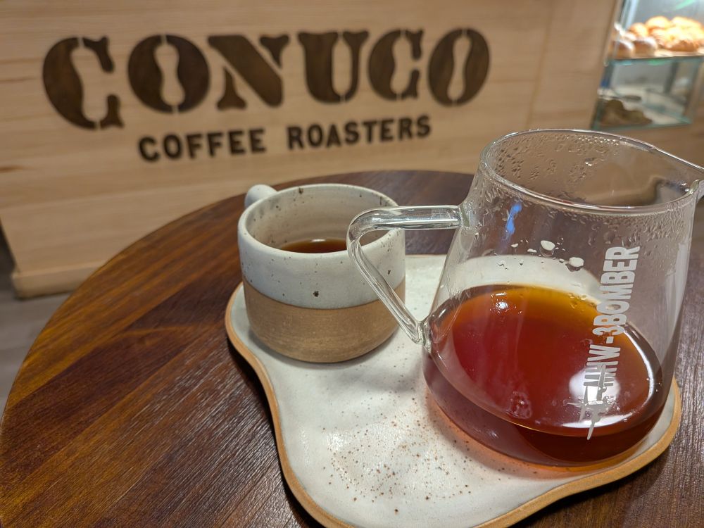 Coffee mug and server in front of a counter reading Conuco Coffee Roasters