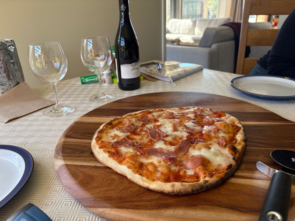 Steaming hot pizza on the board ready to cut with wine ready to pour.