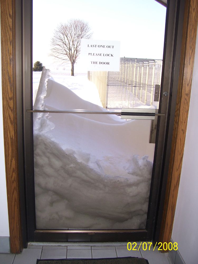 Terrible picture of a tree in the snow. Picture is out a glass door with snow coming up about a third of the way with a sign on the door "Last one out, please lock the door". The tree is in the background to the left of the sign. There are no leaves, being winter and all, but it is still the perfect tree. Also in the photo are dog kennels on the right and the date 02/07/2008 down in the right lower corner that marks it as taken before time began.