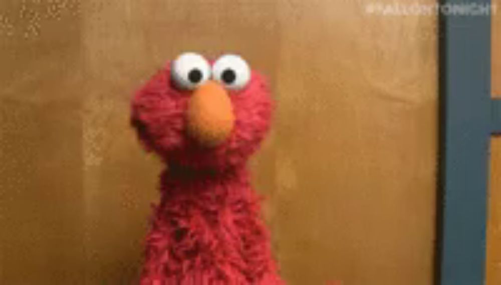 elmo from sesame street is standing in front of a wall .