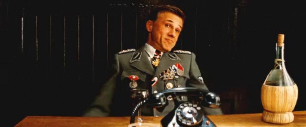 a man in a military uniform is sitting at a table with his arms outstretched next to a telephone