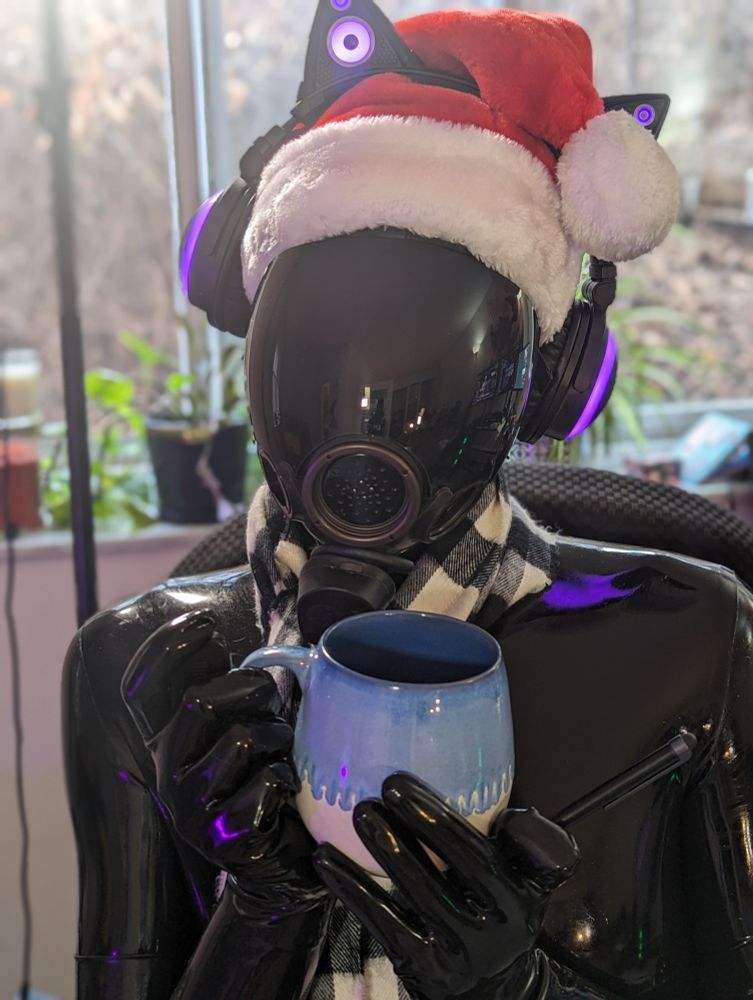 A festive HexDrone is holding a baby blue mug and a pen. The latex has a purple reflection, and the Drone is wearing a red Santa hat along with a checkered black and white scarf.

The mug is probably empty. That would make sense, since drinking through a gas mask isn't economical. They do come with straws, though. Happy Holidays!!