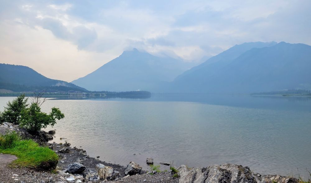A photo of the mountains appearing out of the haze with Lac Des Arcs in the foreground.