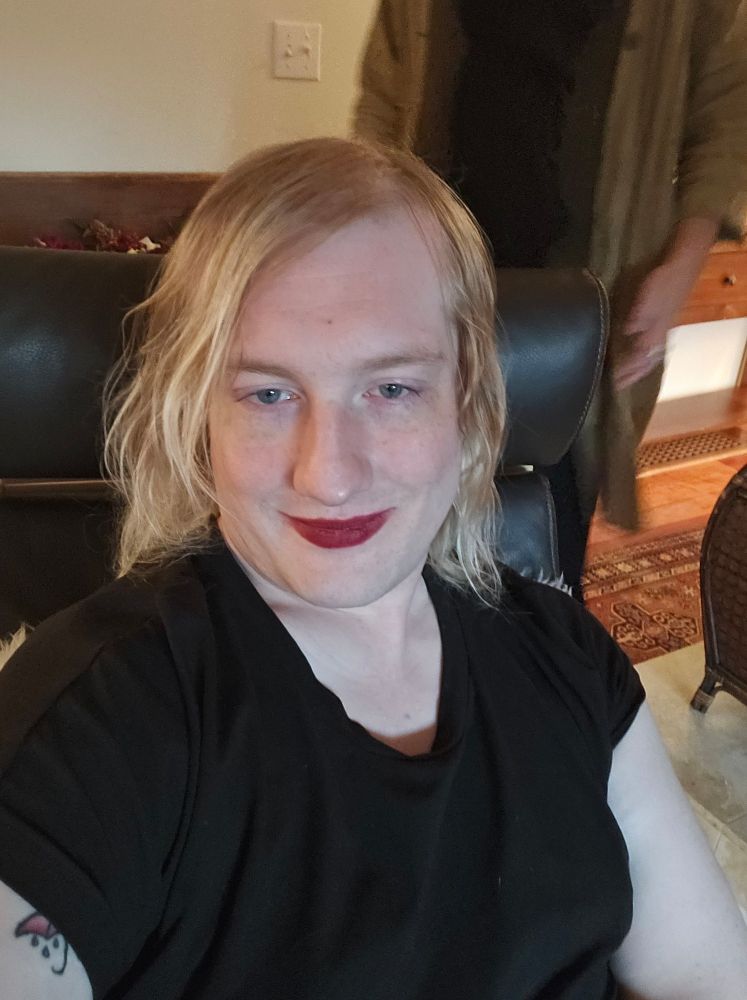 Image of a blonde girl in a black dress sitting in a chair smiling. She has red lipstick on.