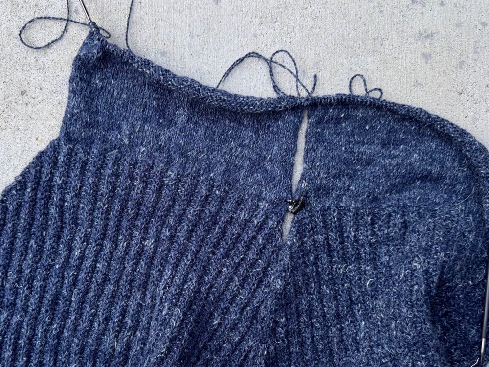 Dark blue knitted bits that will be sleeves, laid flat on a concrete background, with texture in the lower parts (this sweater is based on saddle shoulder military sweaters)