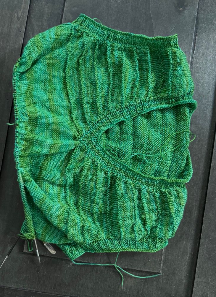 A variegated bright green v-neck sleeveless knit with some purl rows, laid flat on a dark background
