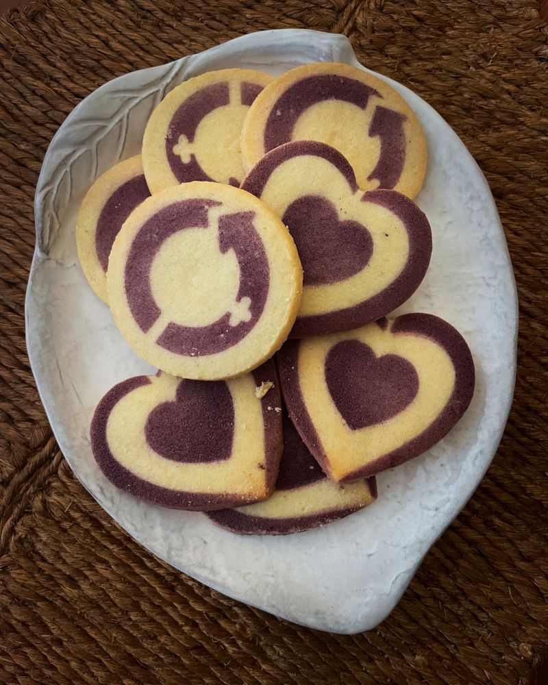 Round sugar cookies with the purple International Women’s Day logo and heart shaped sugar cookies also with purple pattern. 