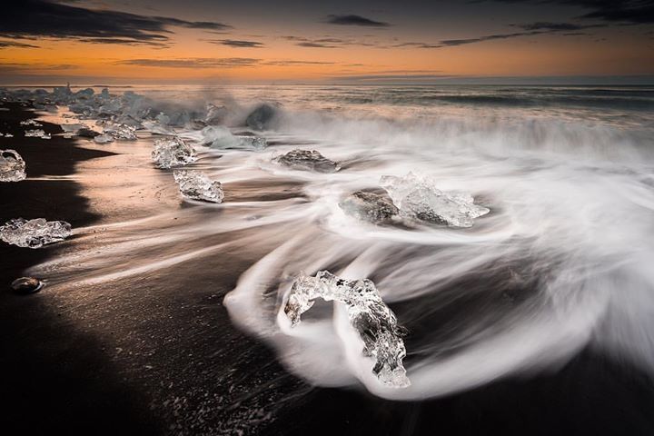 Icelandic landscape photography showing ice glaciers the size of large boulders engulfed by waves hitting a beach in Iceland.