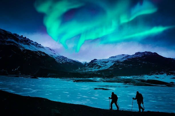The green and blue Northern Lights or Aurora Borealis are visible in the sky above at a lagoon or lake in Iceland at night. 