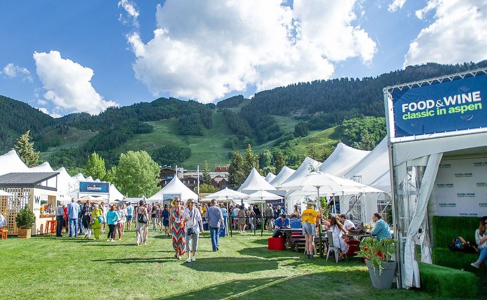 Photos of different booths at the famous Food and Wine festival in Aspen. The white-tented booths are set against a gorgeous backdrop of lush, green, forest-filled Colorado mountains and bright, sunny blue skies dotted with white clouds. 