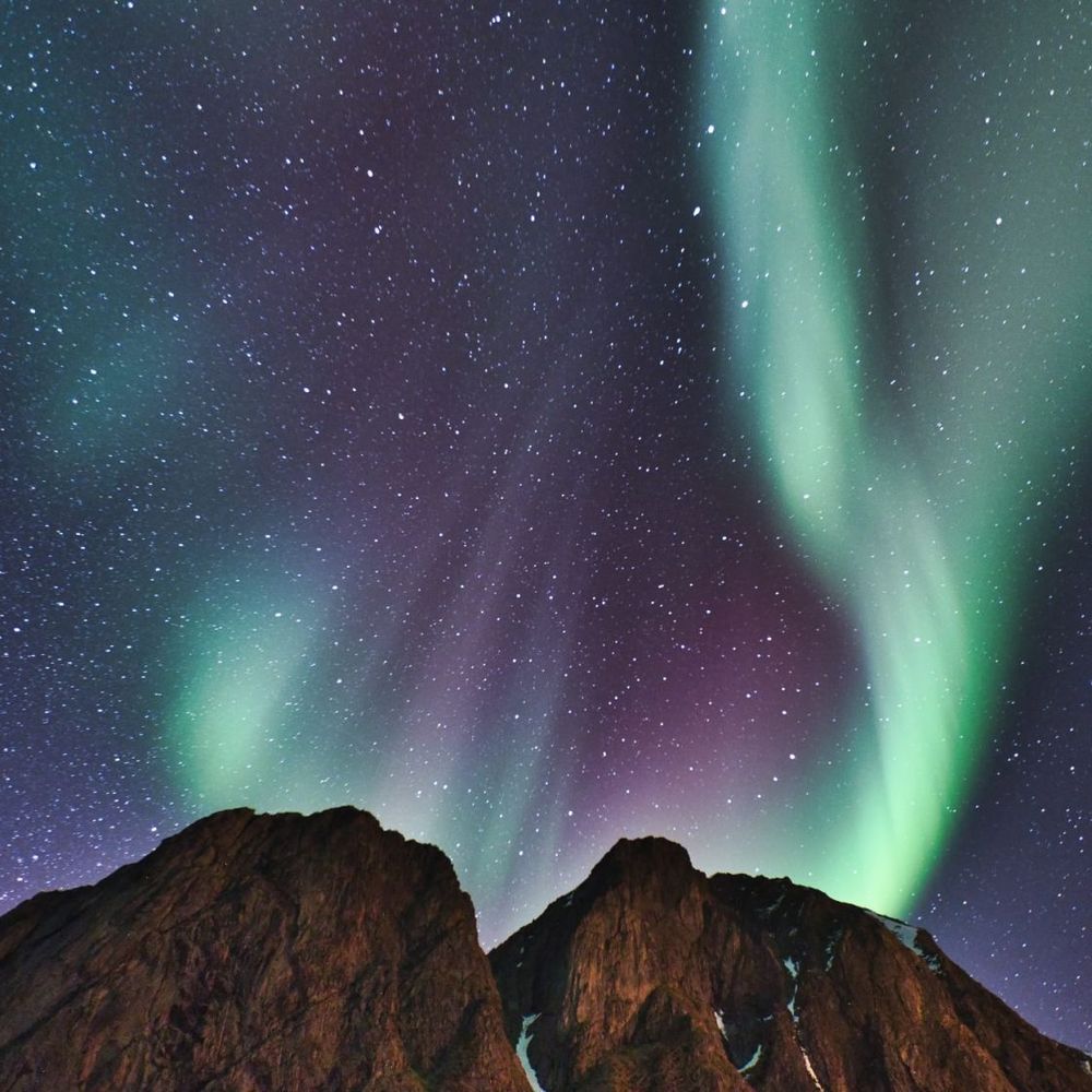 Green and purple northern lights above a dark Icelandic mountain ridge.