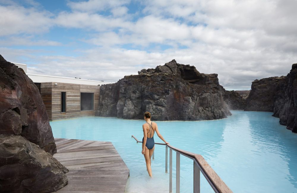 A woman holds onto a railing on a walkway that leads into the steaming, hot, turquoise waters of Iceland's famous Blue Lagoon.