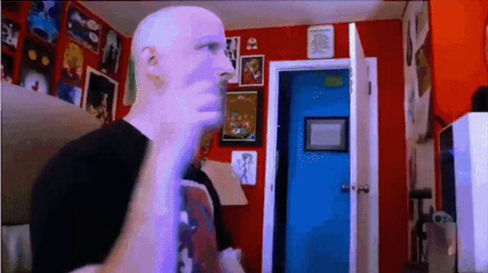 a bald man in a black shirt is standing in a room with red walls and a blue door