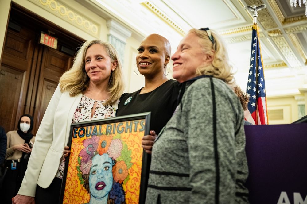 Congresswomen Ayanna Pressley and Abigail Spanberger pose for a photo with Congresswoman Spanberger's mother holding a sign that reads Equal Rights.