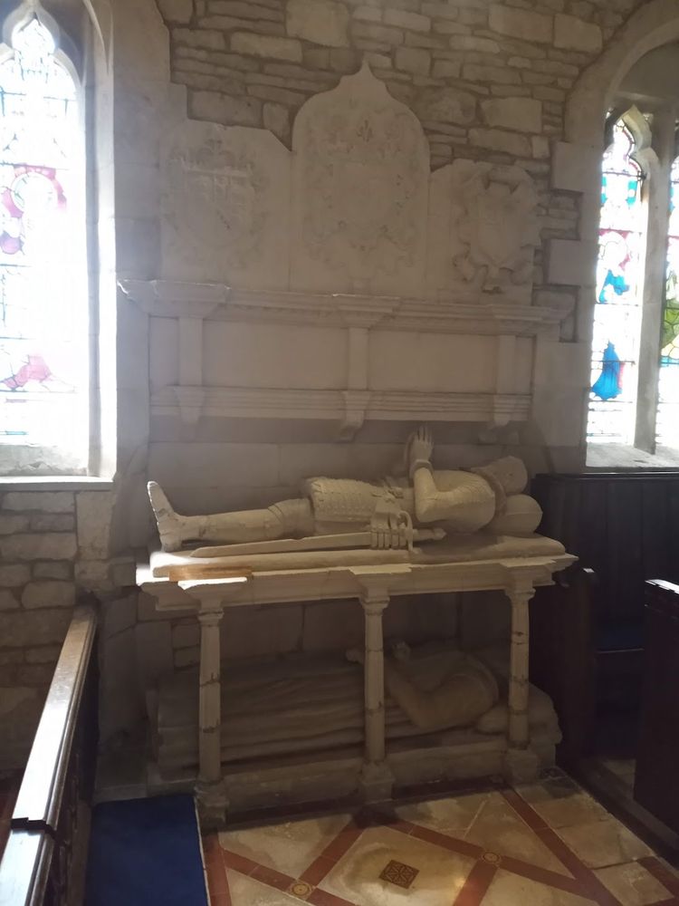 Church monument. Two effigies of men, c1585, one above the other the lower dressed in long robes being enclosed within an open-sided tomb flanked by fluted columns, the upper dressed in armour. Large limestone overmantel with three heraldic shields over. 