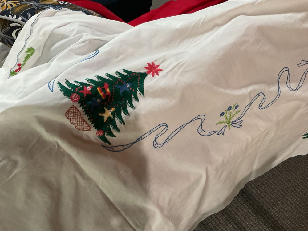 White table cloth with green Christmas tree and blue ribbons and flowers all stitched by hand