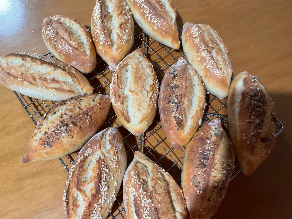 Small crusty bread rolls on a cooling rack..some with sesame seed and some with mixed seeds on top
